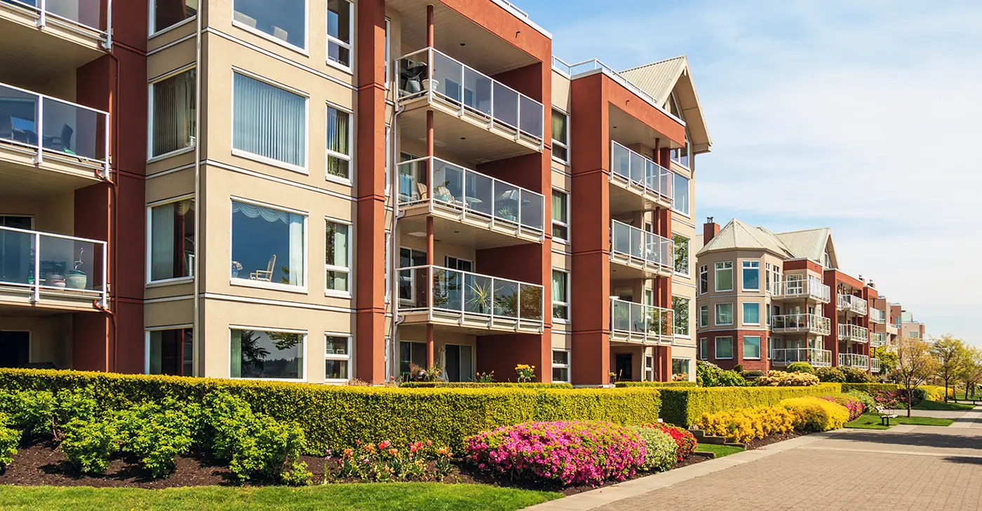 Modern mid-rise apartment buildings with glass balconies and landscaped hedges